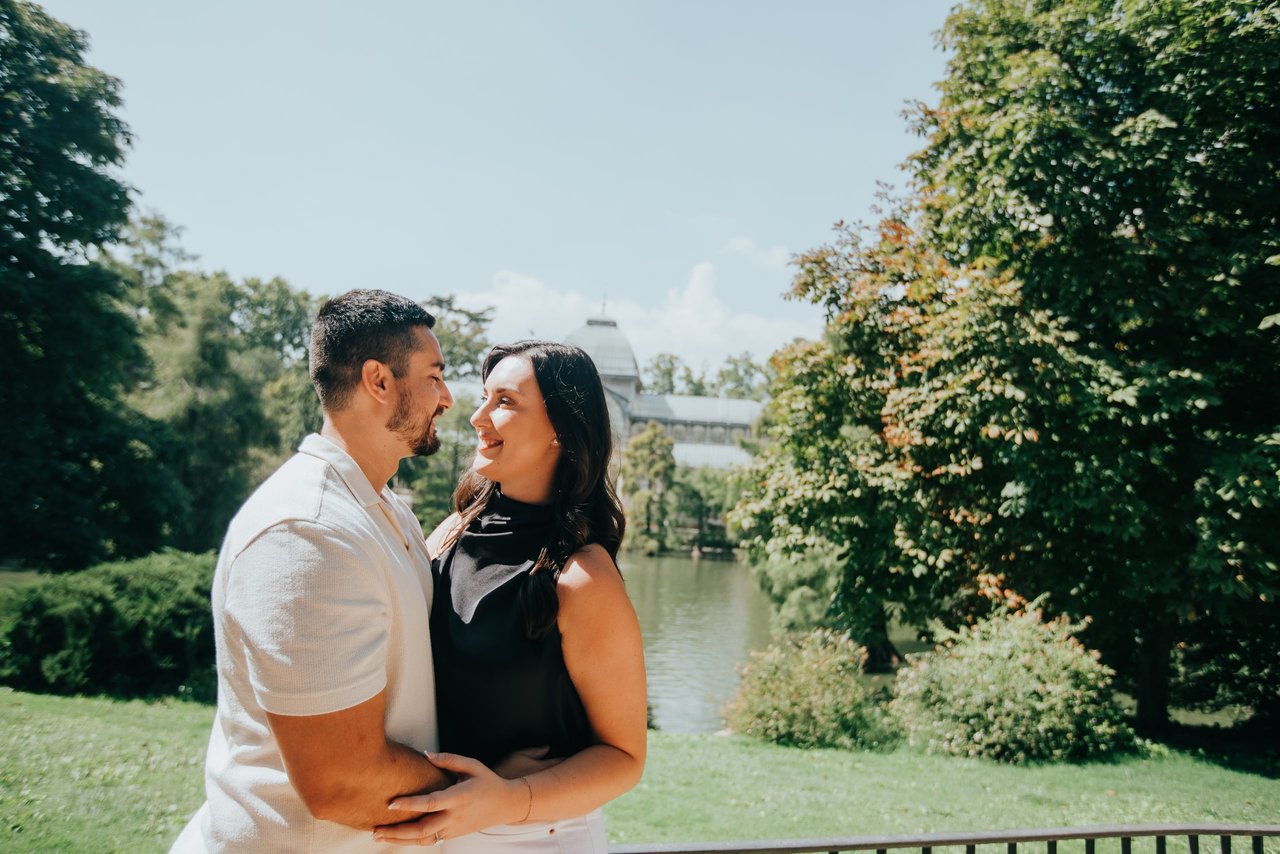 Couple embracing by a riverside garden with ivy-covered walls and a distant bridge in Madrid
