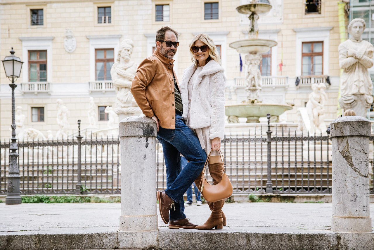 Couple posing at Fontana Pretoria in Palermo, with ornate palazzo and marble statues in background