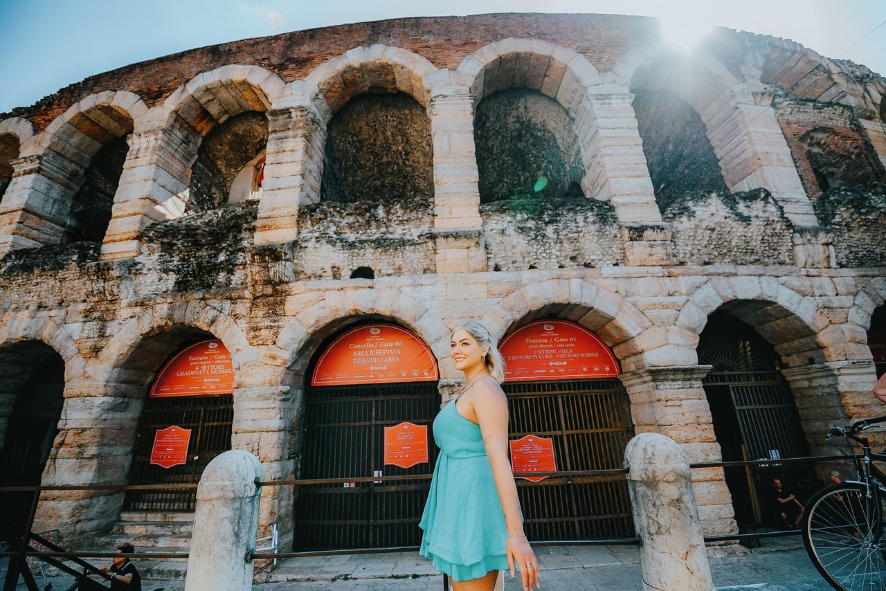Woman in turquoise dress posing at ancient Roman amphitheater with arched facade in daylight