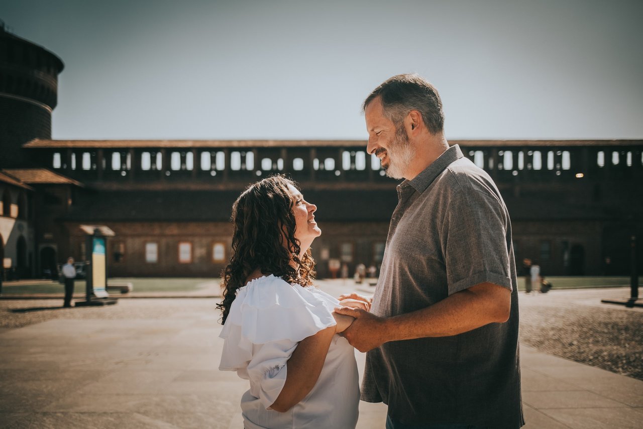 Couple smiling together in sunlit courtyard at Sforzesco Castle in Milan
