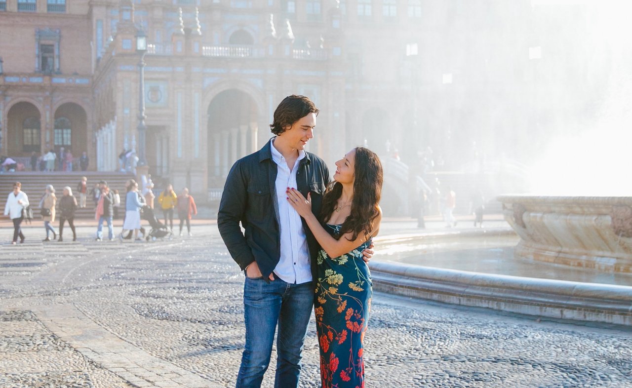 Couple embracing in golden morning light at a historic Seville plaza with baroque architecture behind them