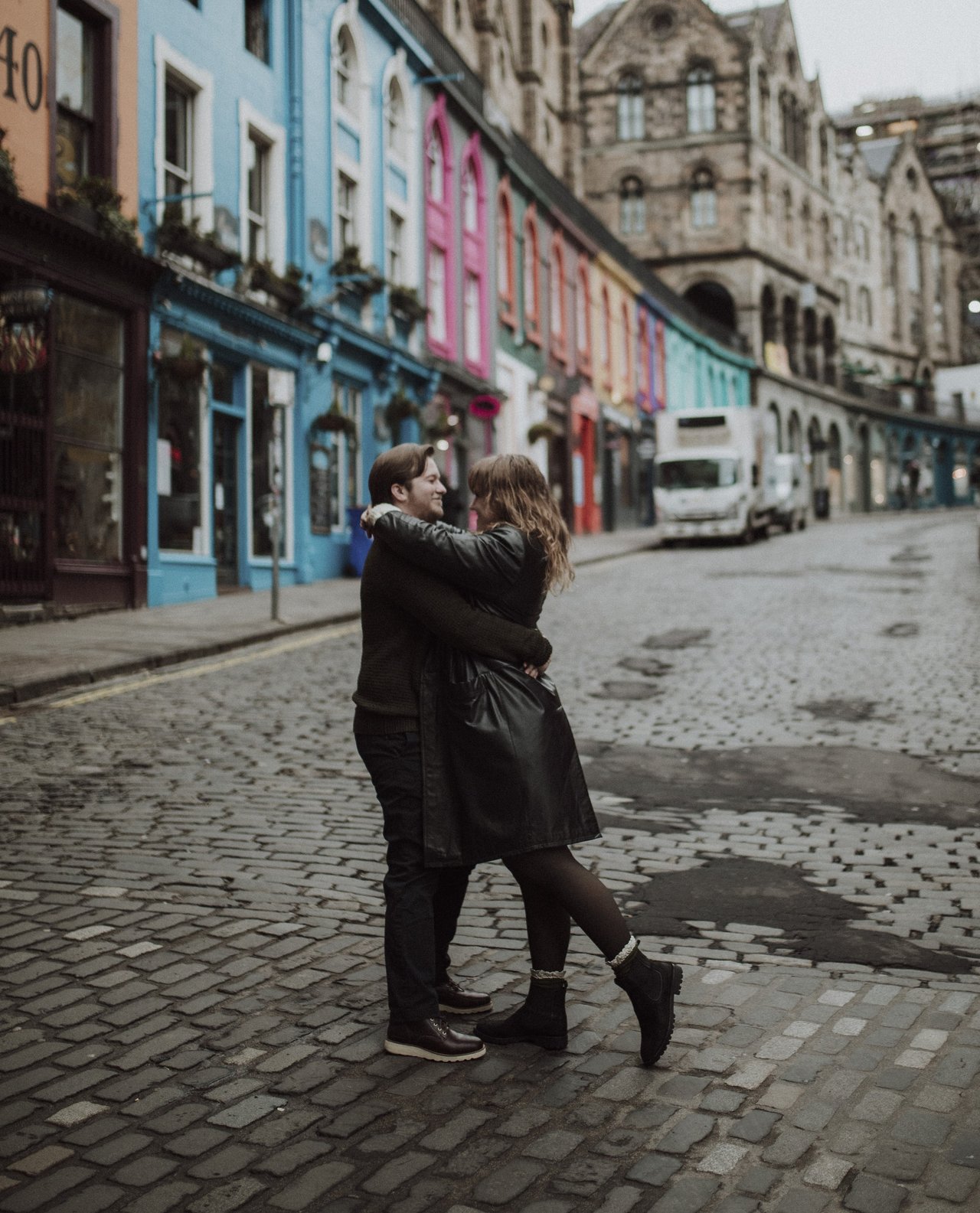Couple embracing on a cobblestone street lined with colorful buildings in Edinburgh's historic old town