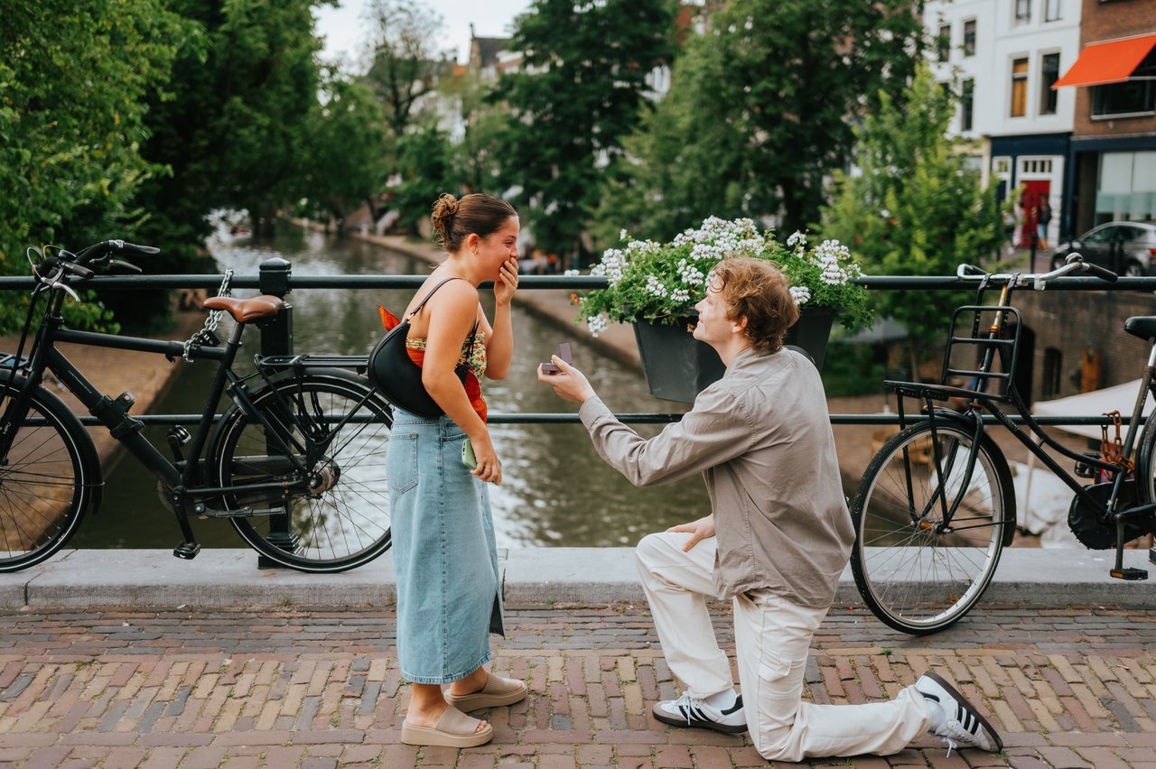 Man on one knee proposing to woman on canal-side bridge in Utrecht during daytime