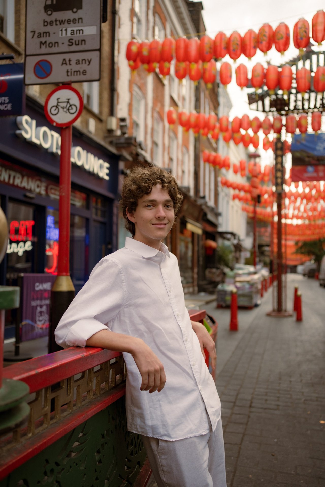 Solo traveler in white shirt posing on London street with red lanterns strung overhead during daytime