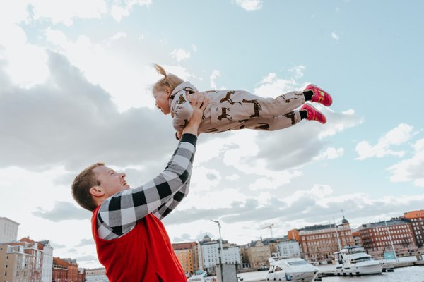 Father lifting young child above his head with Helsinki waterfront and colorful buildings behind them