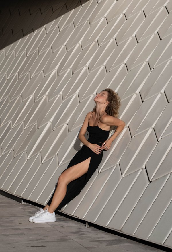Woman in black outfit posed against geometric white ribbed wall in bright sunlight