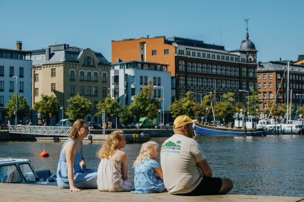 Family of four sitting on dock overlooking colorful waterfront buildings and boats in Helsinki
