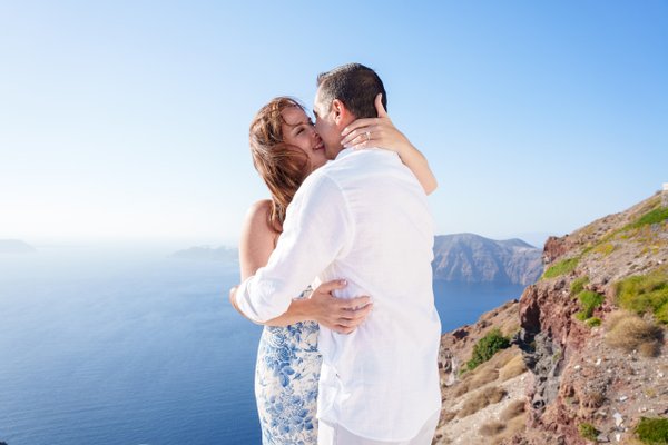 Couple embracing on a clifftop overlooking the sea and mountains in bright daylight