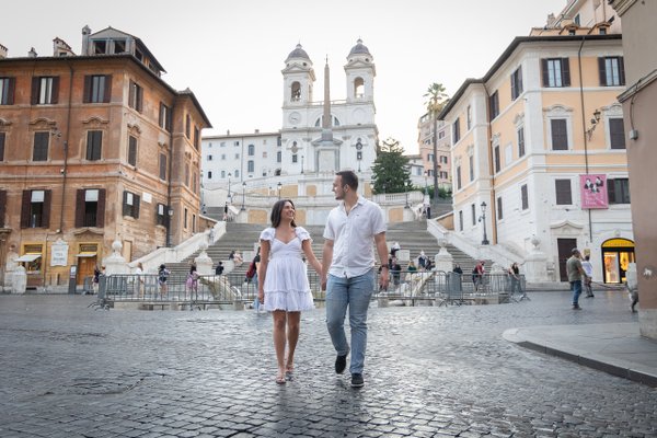 Couple walking hand in hand at the Spanish Steps in Rome during daytime with twin-towered church in background