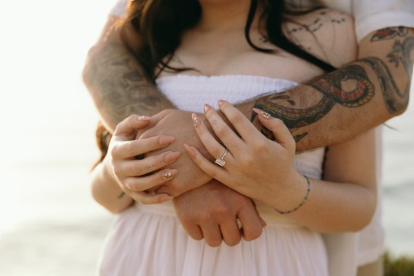 Couple displaying wedding rings and tattoos in close embrace during golden hour photoshoot