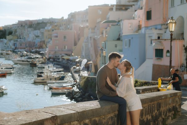 couple kissing on waterfront wall overlooking colorful pastel houses and moored boats at golden hour