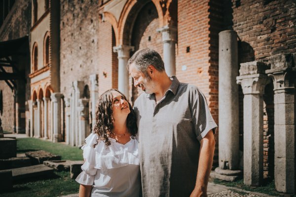 Couple smiling at each other in sunlit courtyard with red brick arches and classical columns
