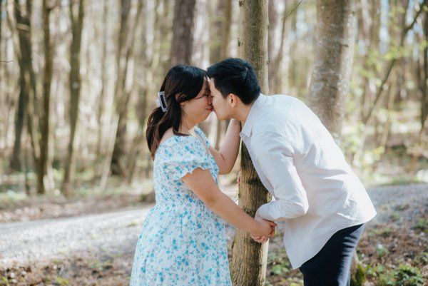 couple kissing by tree in sunlit forest during daytime