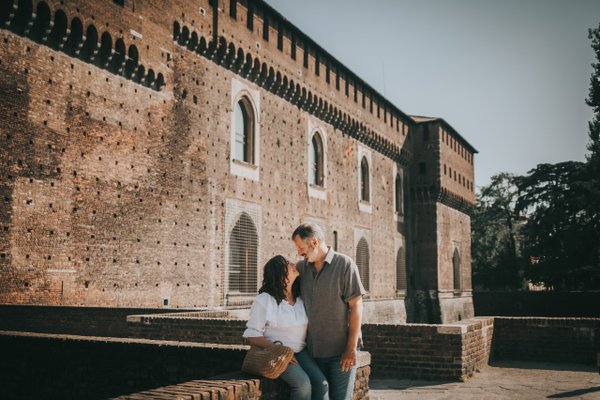 couple posing by historic brick castle with crenellated towers in golden afternoon light