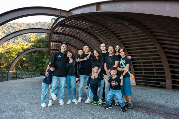 large family group posing under curved modern architecture with forested hills and water visible in background