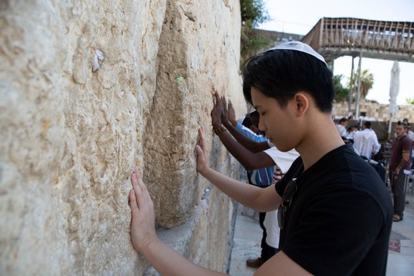 solo traveler touching ancient stone wall at Western Wall, Jerusalem in daylight