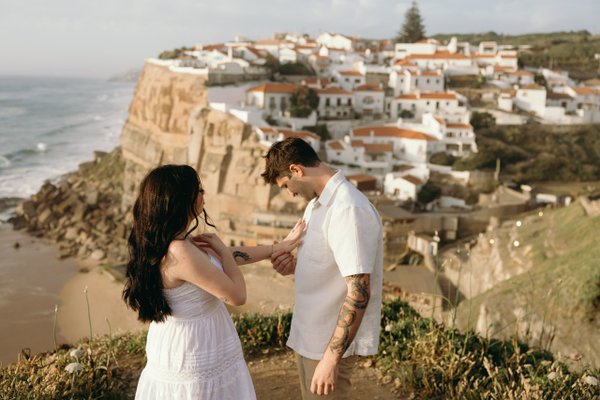 Couple in white outfits overlooking clifftop village of Azenhas do Mar at golden hour, Portugal