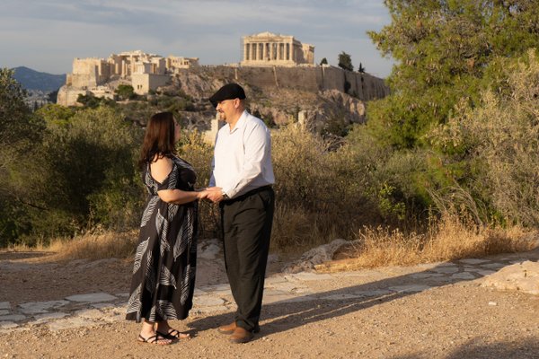 Couple holding hands on a dusty path with the Acropolis in golden afternoon light behind them