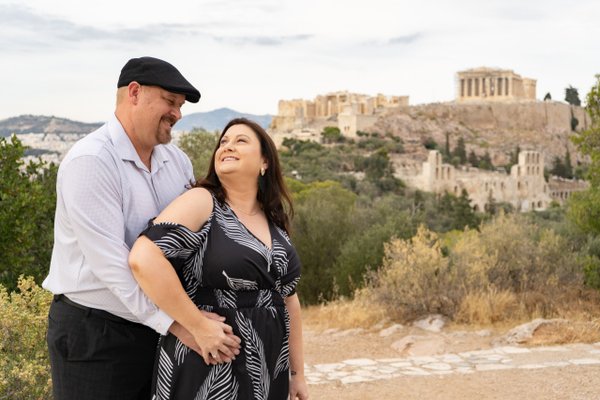 Couple posing together with the Parthenon and Athens acropolis visible in the background during daytime