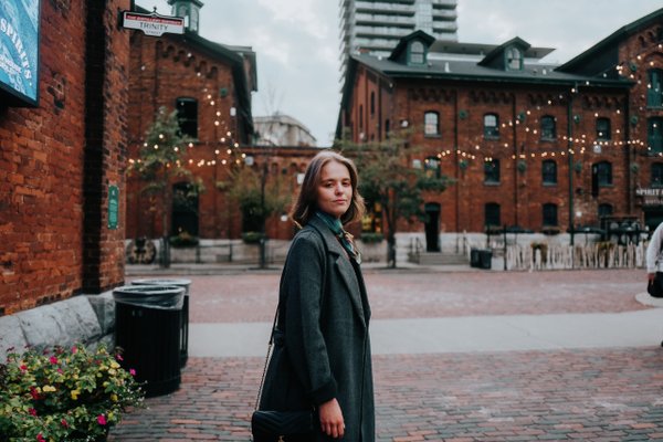 Solo traveler in dark coat at festive Distillery District, surrounded by red brick buildings and holiday lights