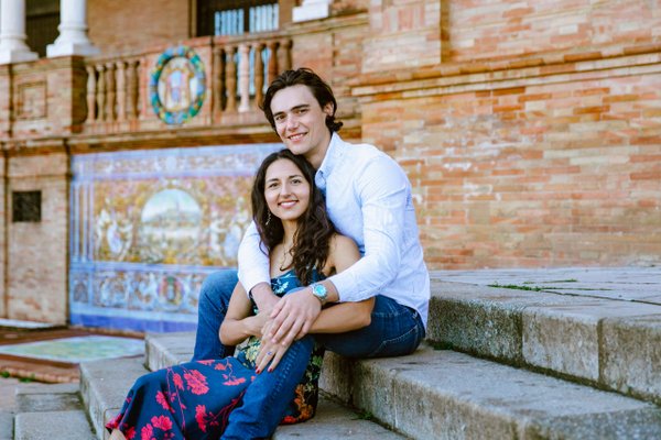 Couple seated on steps against colorful blue tiled brick building facade in daylight