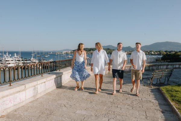 Family of four walking along waterfront promenade with sailboats and mountains in afternoon light