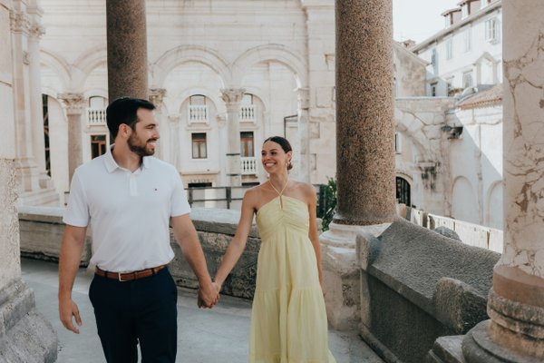 Couple holding hands at Peristyle in Split, walking past ancient Roman columns in warm daylight