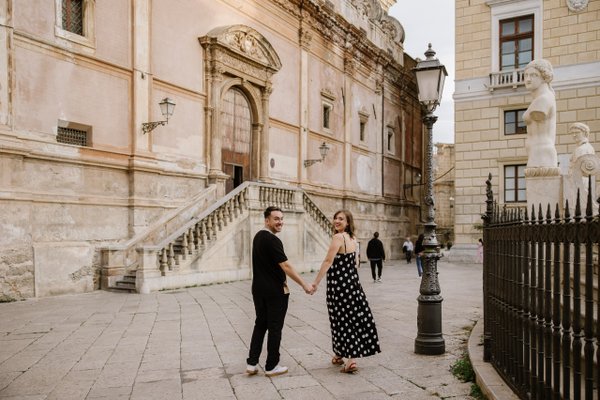 Couple holding hands in a historic Palermo square with classical architecture and marble statues