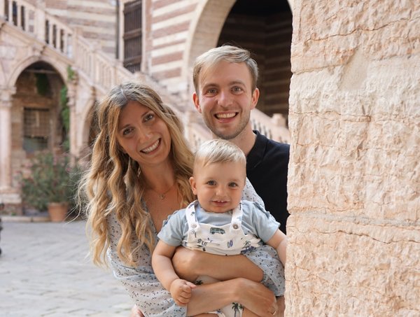 Family of three smiling in a sunlit medieval stone courtyard with arched architecture in Verona