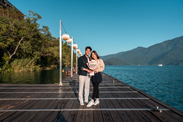 Couple standing on a wooden pier at Sun Moon Lake with mountains and blue water in bright daylight