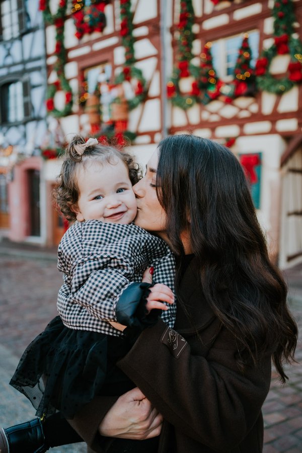 Mother and toddler smiling at festive holiday decorations on a historic half-timbered building in Colmar