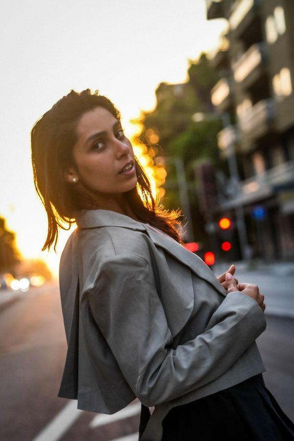 Woman in grey blazer on urban street at golden hour sunset with blurred architecture behind