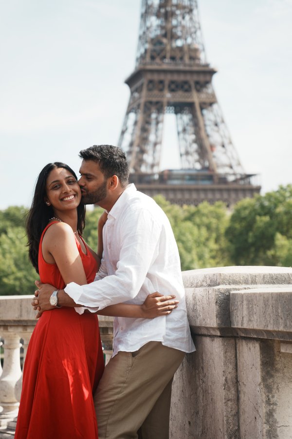Couple posing at a stone ledge with the Eiffel Tower behind them on a sunny day in Paris