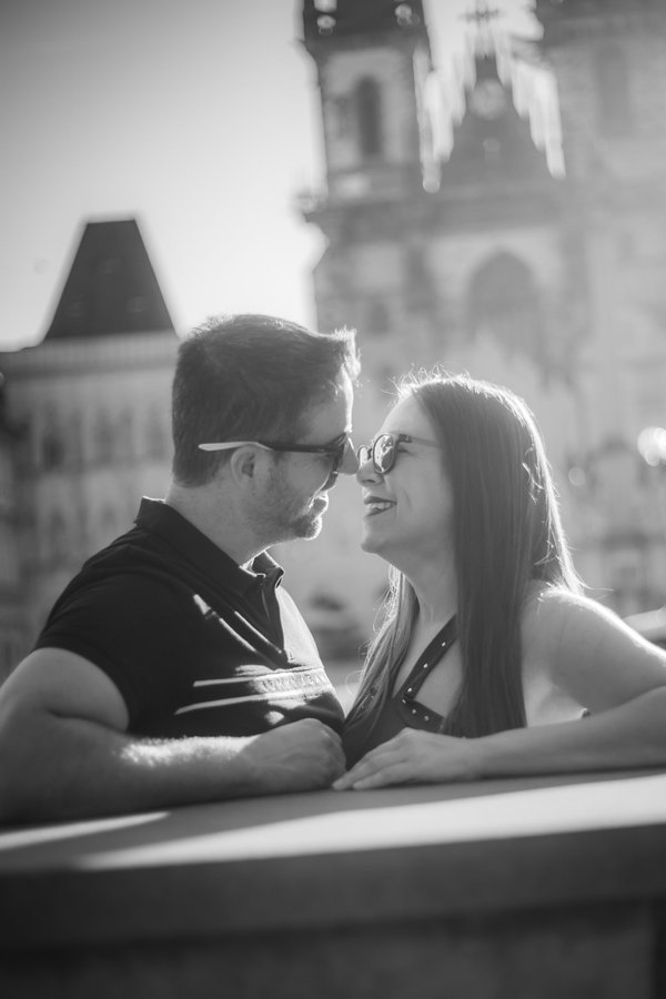 Couple in sunglasses smiling at each other during golden hour with Prague's historic architecture blurred in background