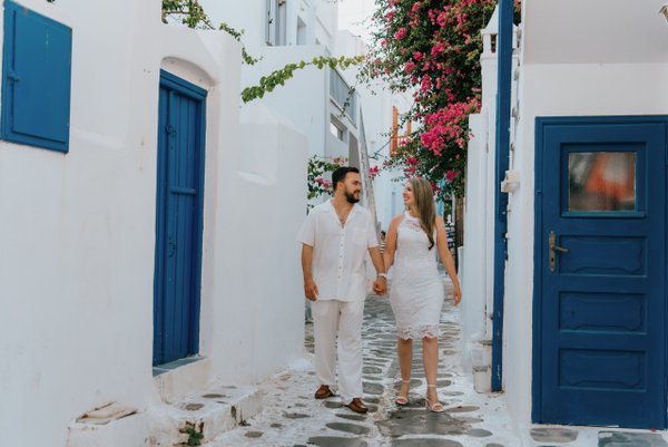 couple walking hand in hand through whitewashed alley with blue doors and pink bougainvillea in mykonos