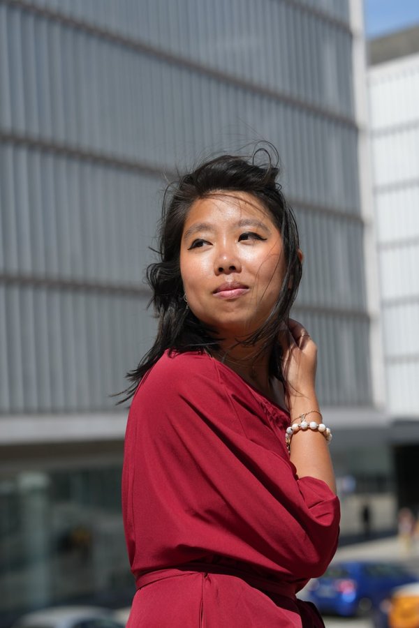 Solo traveler in red dress posing at modern architecture, bright daylight