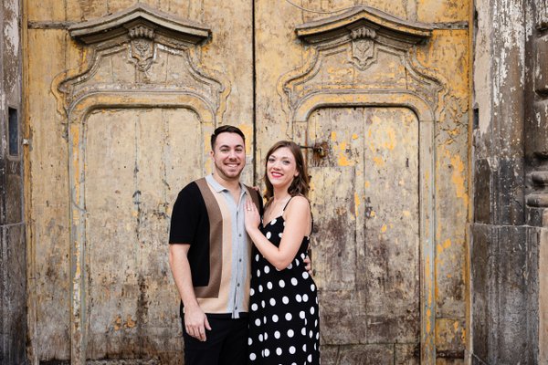Couple smiling in front of ornate weathered golden doors in historic Palermo
