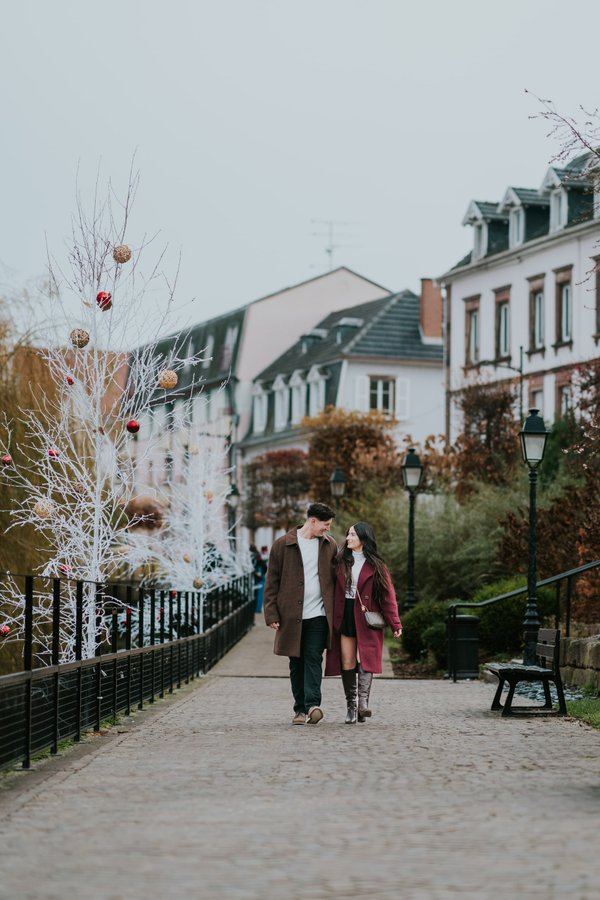 Couple walking through festive European street with white ornament-decorated tree and historic architecture in Colmar