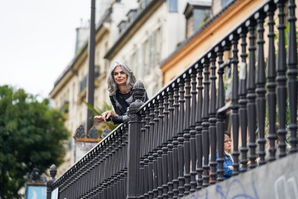 Woman with gray hair leaning on ornate black railing on Parisian building balcony, daytime