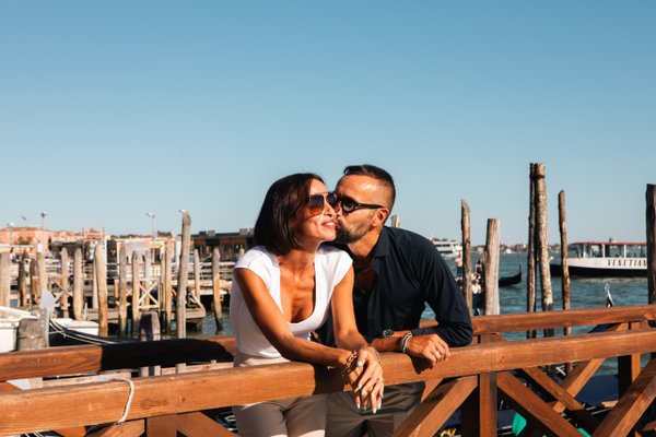 Couple kissing on wooden dock overlooking Venice's historic mooring poles and lagoon in bright daylight
