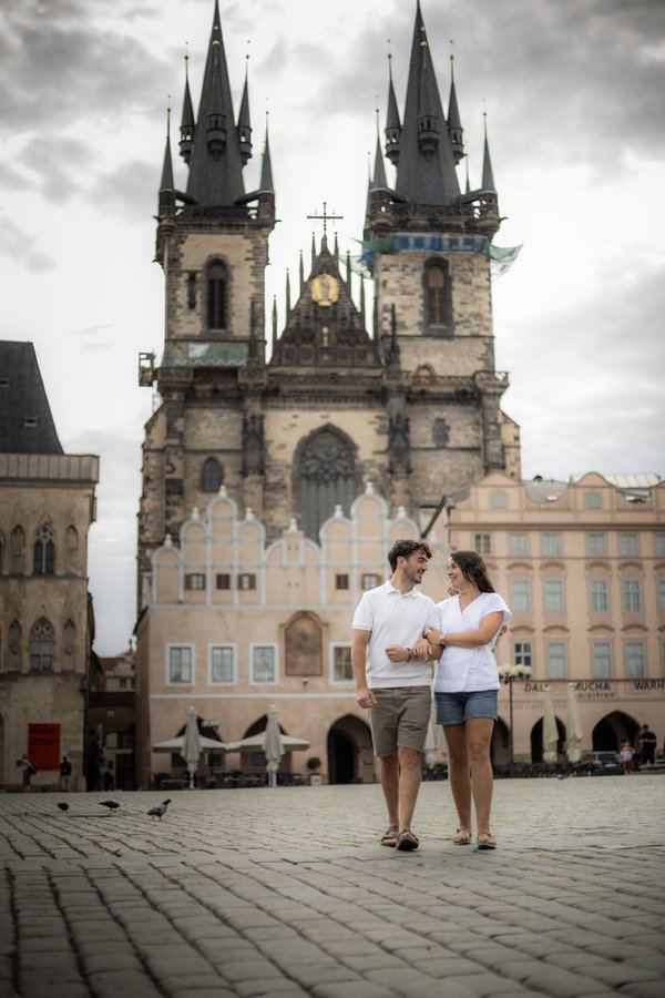 Couple in white shirts standing arm-in-arm in Prague's Old Town Square with the Church of Our Lady before Tyn in the background