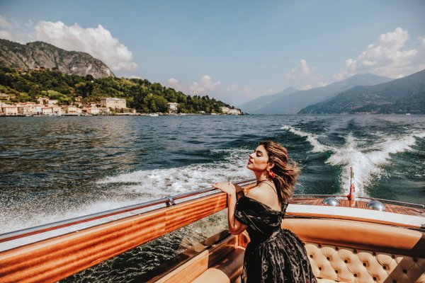 Woman on wooden boat gazing toward lakeside town and mountains on Lake Como during daytime