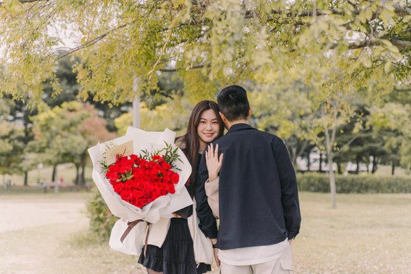 Couple posing under willow tree with red flower bouquet in Seoul park during daytime