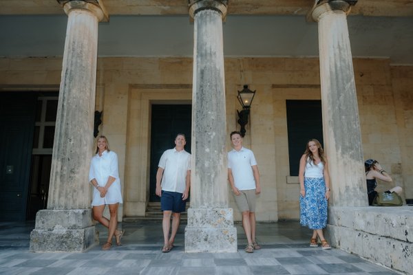 Family of five standing between weathered columns at Spianada Square, Corfu in daylight