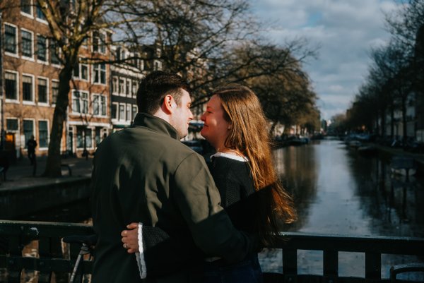 Couple embracing on a bridge over a canal in Utrecht, historic buildings and bare trees reflected in still water