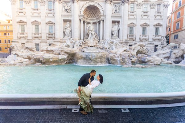 couple poses at the turquoise trevi fountain in rome during daytime with baroque architecture behind