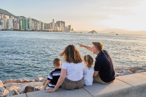 Family of four sitting on waterfront rocks overlooking Hong Kong skyline at sunset