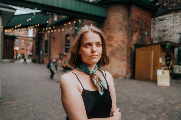 Solo woman in black top at Distillery District's brick courtyard at golden hour with string lights