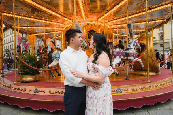 Couple embracing on vintage carousel at golden hour in Florence, warm evening light illuminating ornate ride