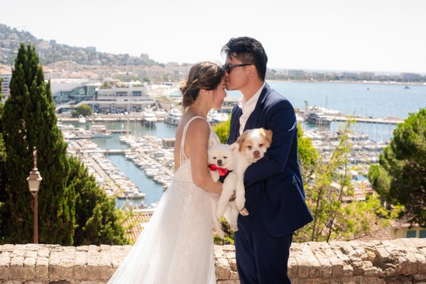 Couple with small white dog overlooking Cannes harbor and yachts from Le Suquet viewpoint in bright daylight